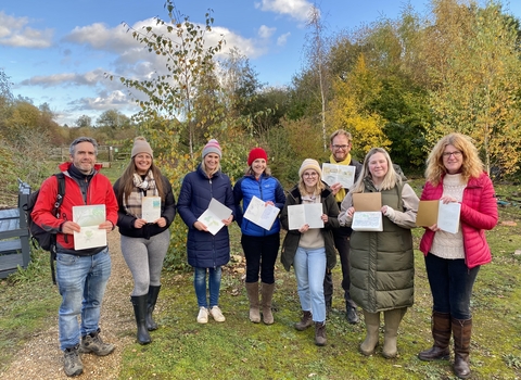 Group of people smiling towards the camera, holding up their open notebooks to display their artwork and journaling