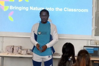Aaron, YPF member standing at the front of a classroom presenting in front of a slideshow titled "Bringing Nature into the Classroom"