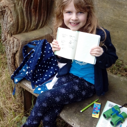 Emma shows off her sketches from a bench at Woodwalton Fen