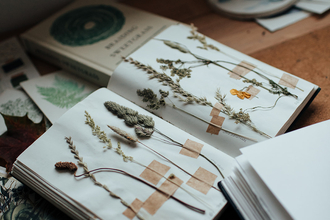 An open sketchbook with wildflower specimens surrounded by creative implements like paint