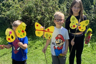 Three children stand holding paper butterflies on sticks