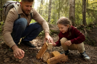 Man with daughter in woodland playing with logs