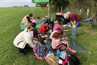 A group of children sit on the floor outside engaged in a wildlife craft activity