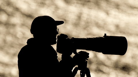 Photographer in silhouette with camera with very big lens