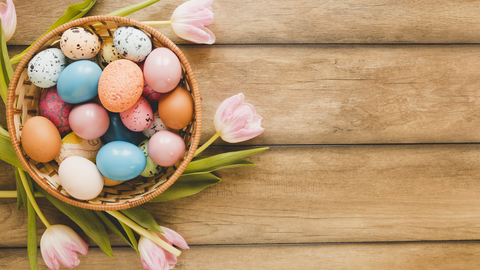 Different coloured eggs in bowl surrounded by tulips