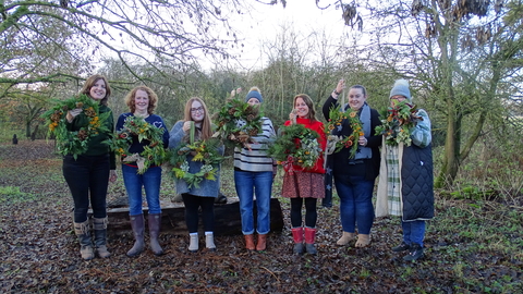 Seven ladies standing outside in winter under trees holding wreaths they've made