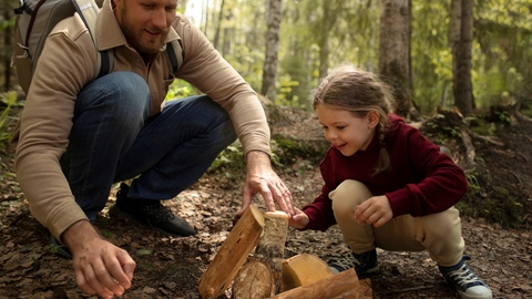 Man with daughter in woodland playing with logs