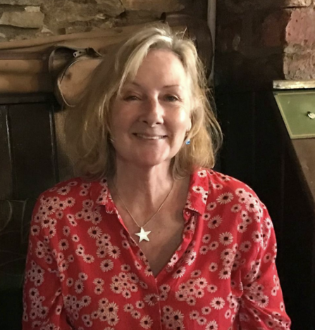 A woman wearing a red, flowery blouse with blonde shoulder-length hair smiles at the camera