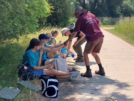 A group sat in the shade on a sunny day, taking a lunch break, with wildlife trust staff handing out tea