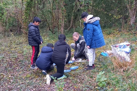 A group of young people learning how to light a fire from a WTBCN staff member in a woodland clearing