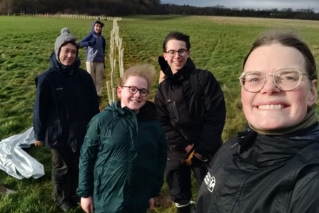 Group of young people smiling at the camera, with WTBCN staff member, in front of a line of planted trees