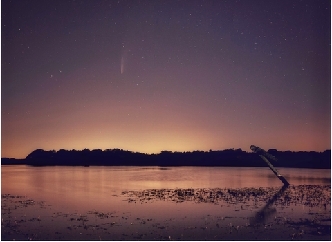 A night-time view over Pitsford Water, with stars in the blue-orange sky and a comet streaking down